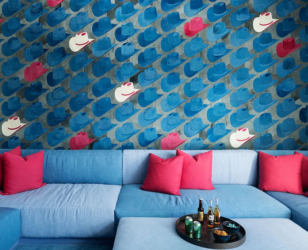Living room with blue sectional sofa, red pillows, and blue and red hat-patterned wallpaper.