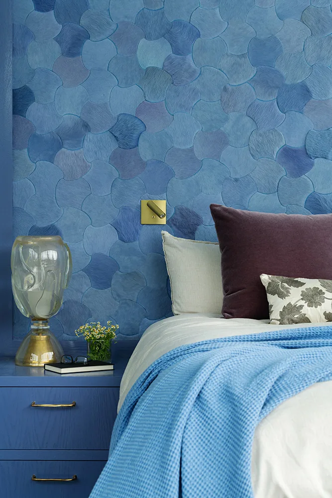 Bedroom corner with blue curvilinear textured wall and a blue nightstand holding a glass lamp and small flowers.