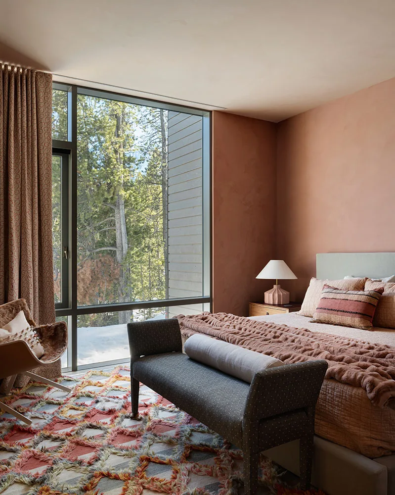 Bedroom featuring a large floor-to-ceiling window to a wooded view, a plush bed, and a patterned area rug.