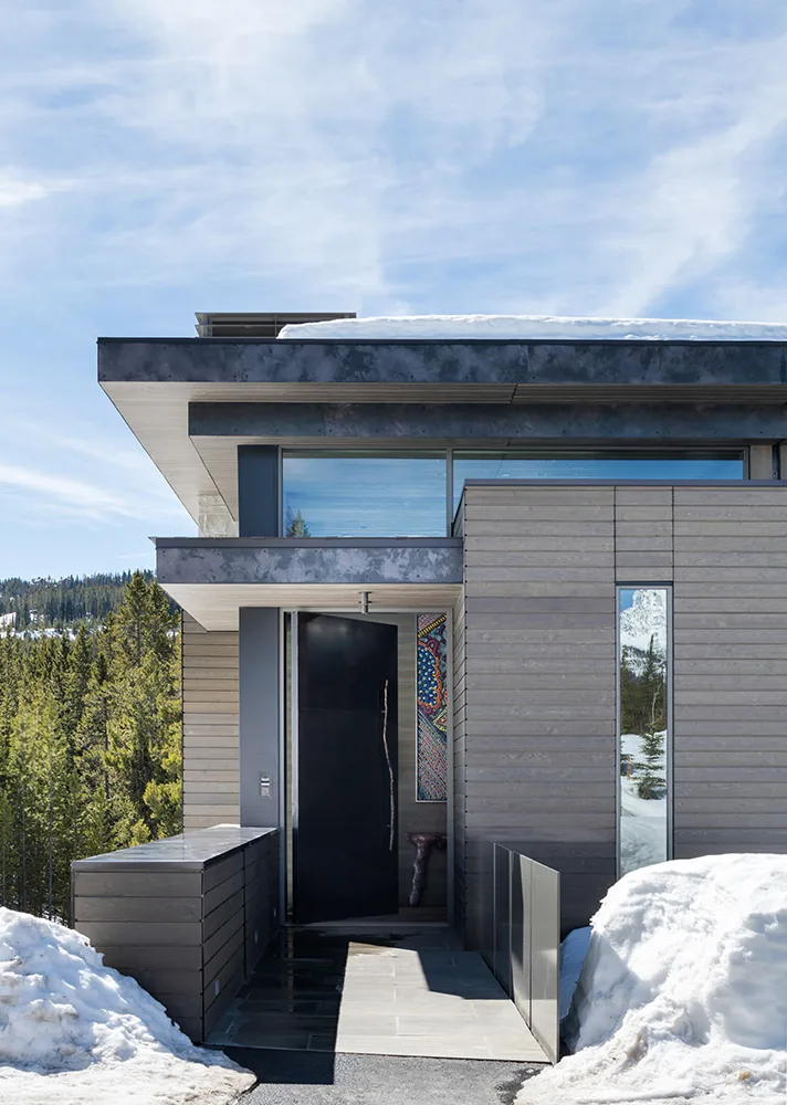 Front entry of Moonlight Basin project with wood siding, large pivot door, and a glimpse of colorful artwork inside.