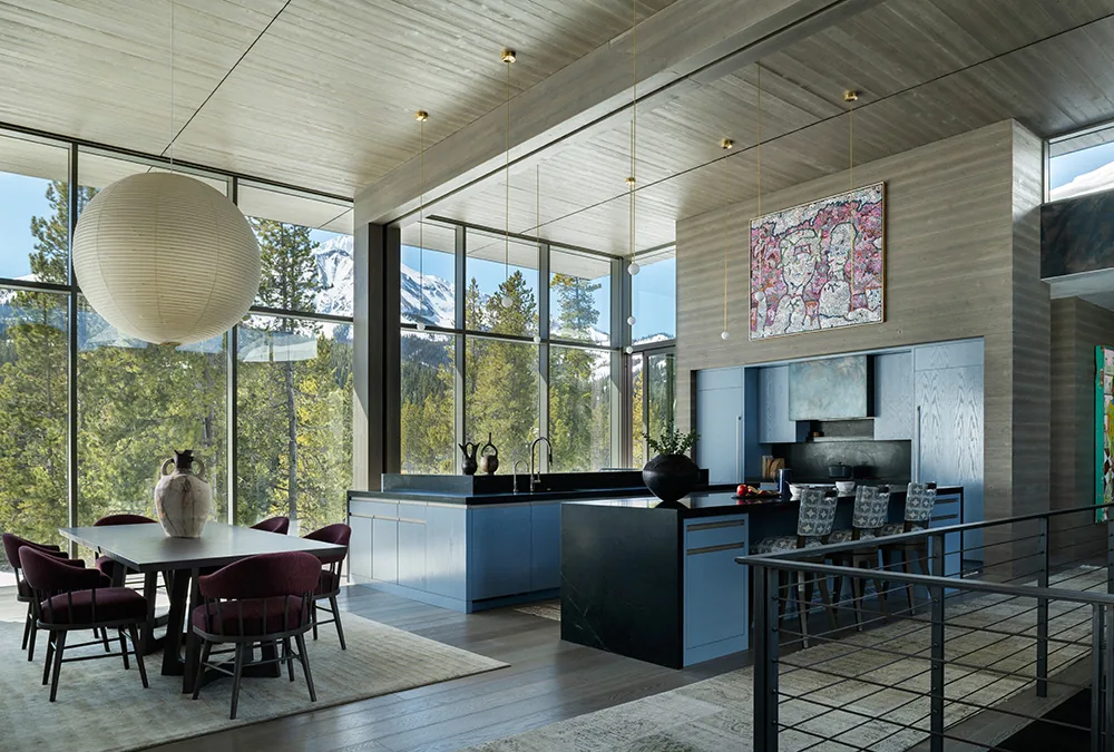 Daylit kitchen with black countertops and blue cabinetry adjacent to dining area featuring purple chairs and paper lantern pendant light.
