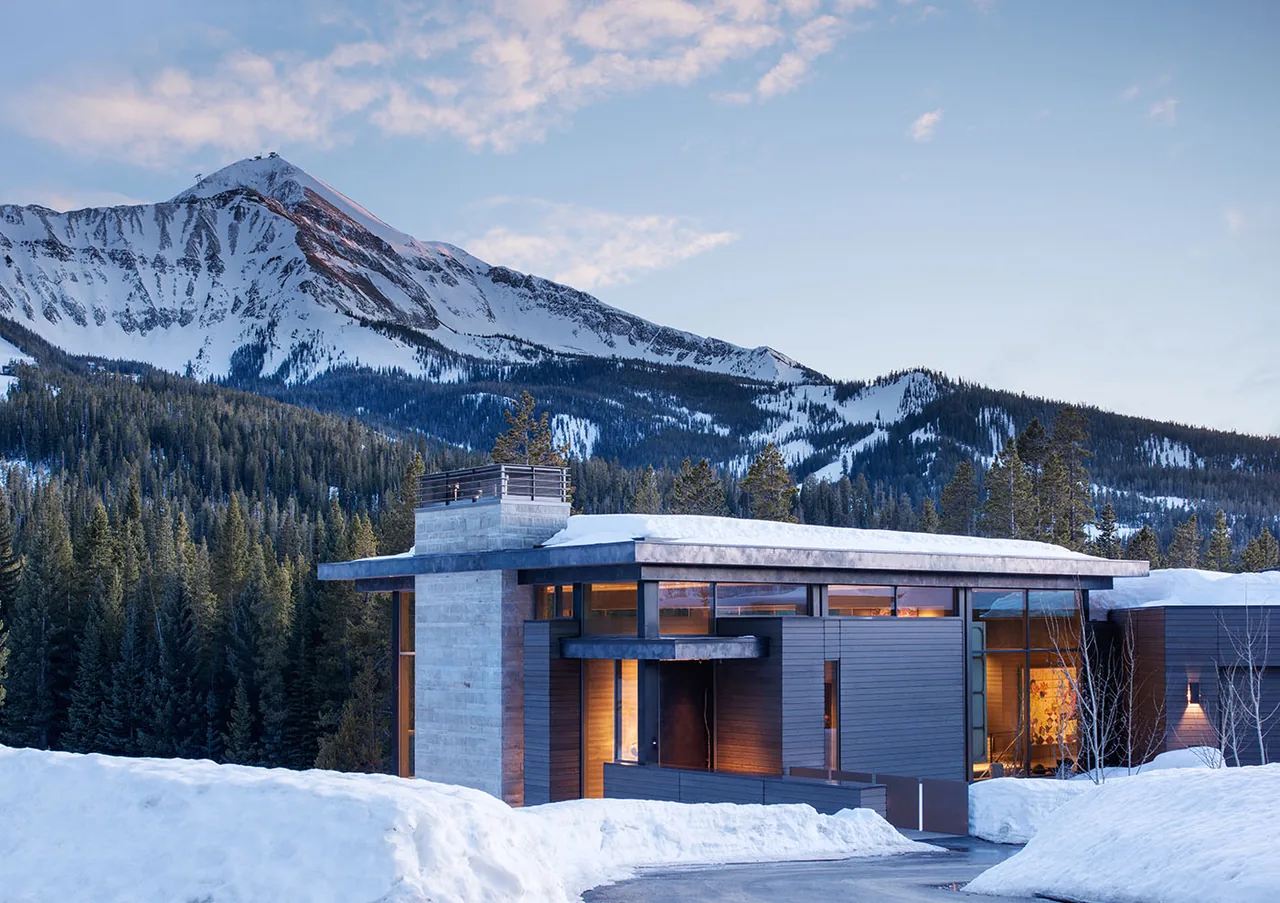 Contemporary single-story home with flat roof and concrete masonry near snow-covered mountains.