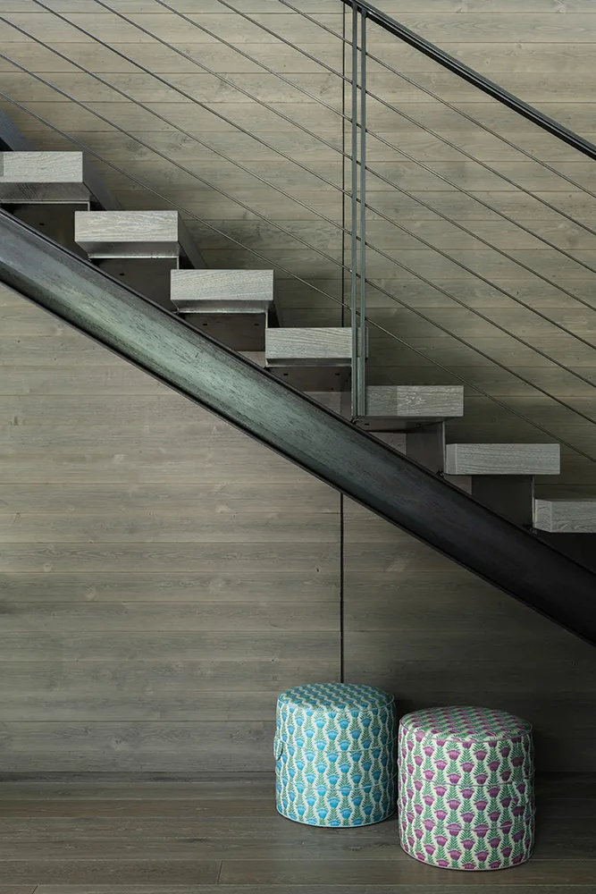 Modern open riser staircase with metal railing and two colorful patterned ottomans below.