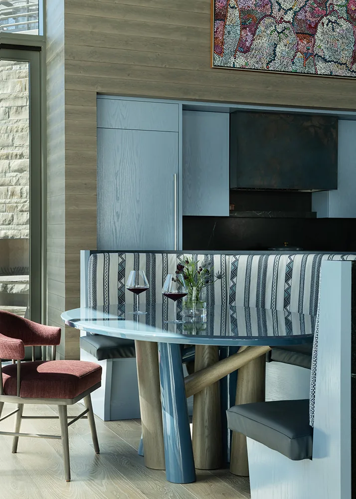 Dining area with an oval glass table, striped upholstered banquette, and a single red chair features modern design elements.