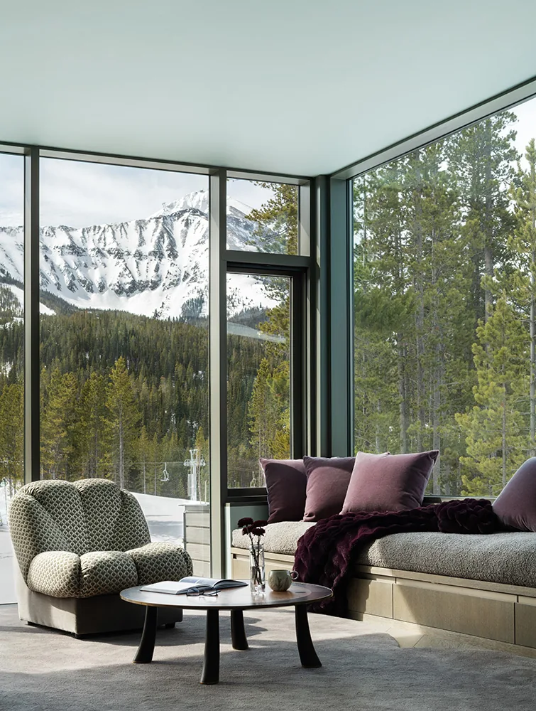 Living room features floor-to-ceiling glazing framing snow-covered mountain and forest views.
