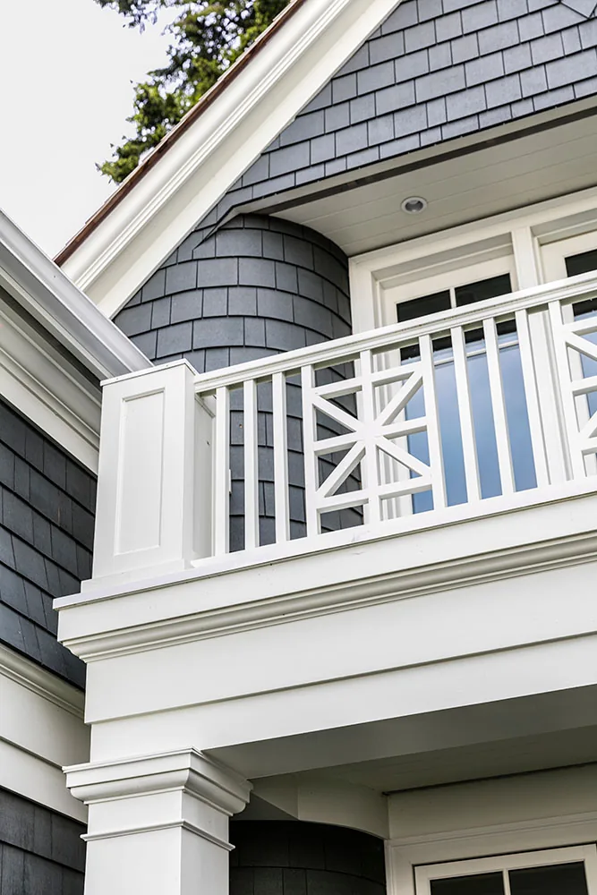 The balcony features white detailed railings and gray shingle siding under multiple gabled roofs.