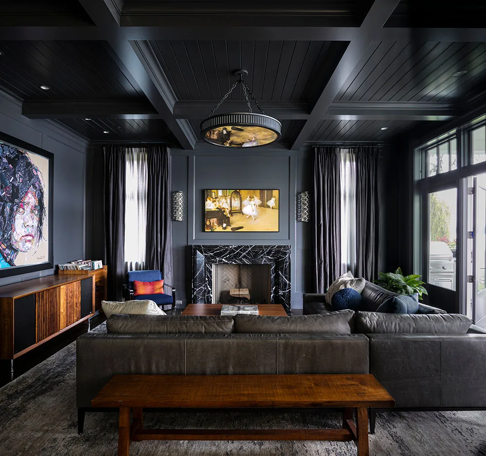 Living room with coffered ceiling, black marble fireplace, and leather sectional sofa facing a large screen.