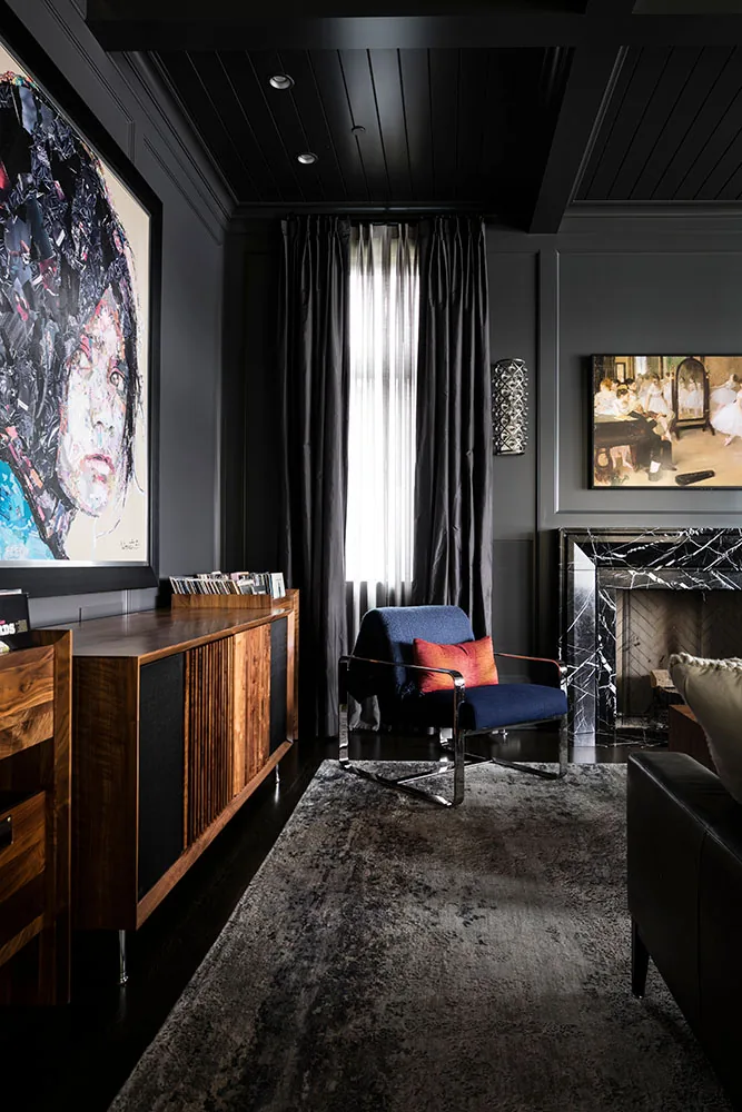 Living room features dark gray walls and ceiling, black marble fireplace, and modern blue armchair with orange pillow.