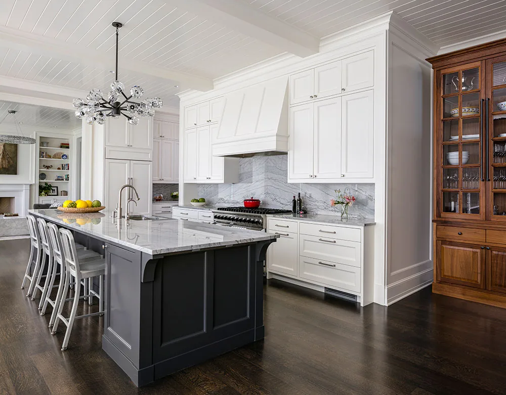 Kitchen featuring a large gray island with marble countertop and white cabinetry with a marble backsplash.