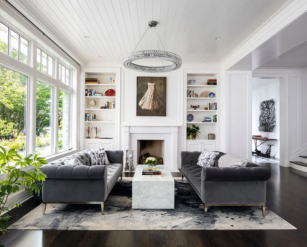 Living room features twin gray tufted sofas, marble coffee table, and built-in bookshelves around a white fireplace.