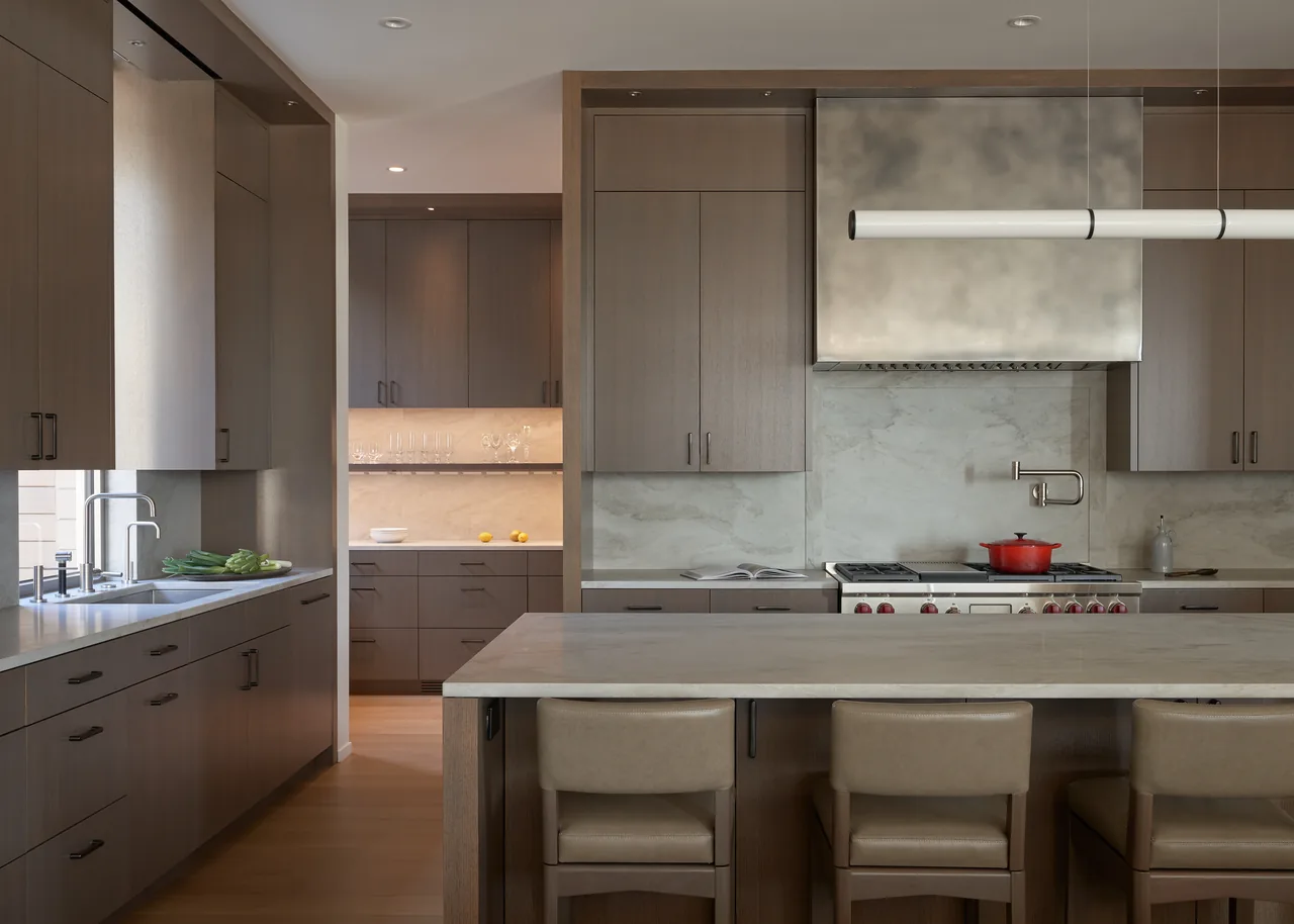 The kitchen of Union Bay Residence features taupe cabinets, marble surfaces, and a built-in gas range with a stainless steel hood.