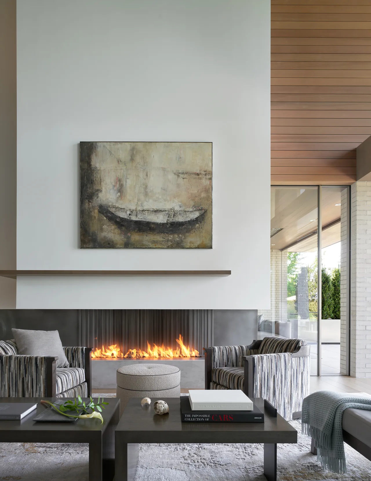 Living room with a linear fireplace, two patterned armchairs, and a large modern painting above the mantel.