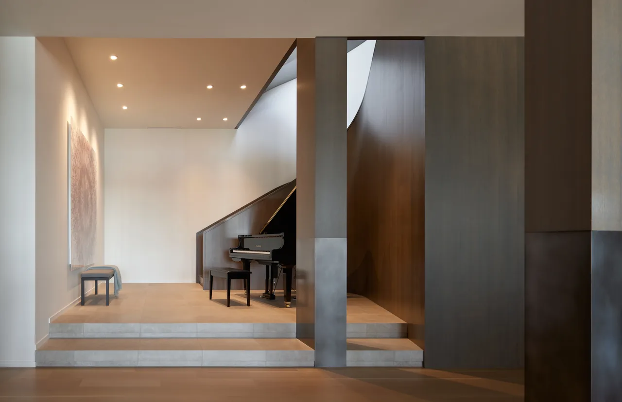 Elevated piano nook with black grand piano beside a wood-paneled curved staircase in a minimalistic interior space.