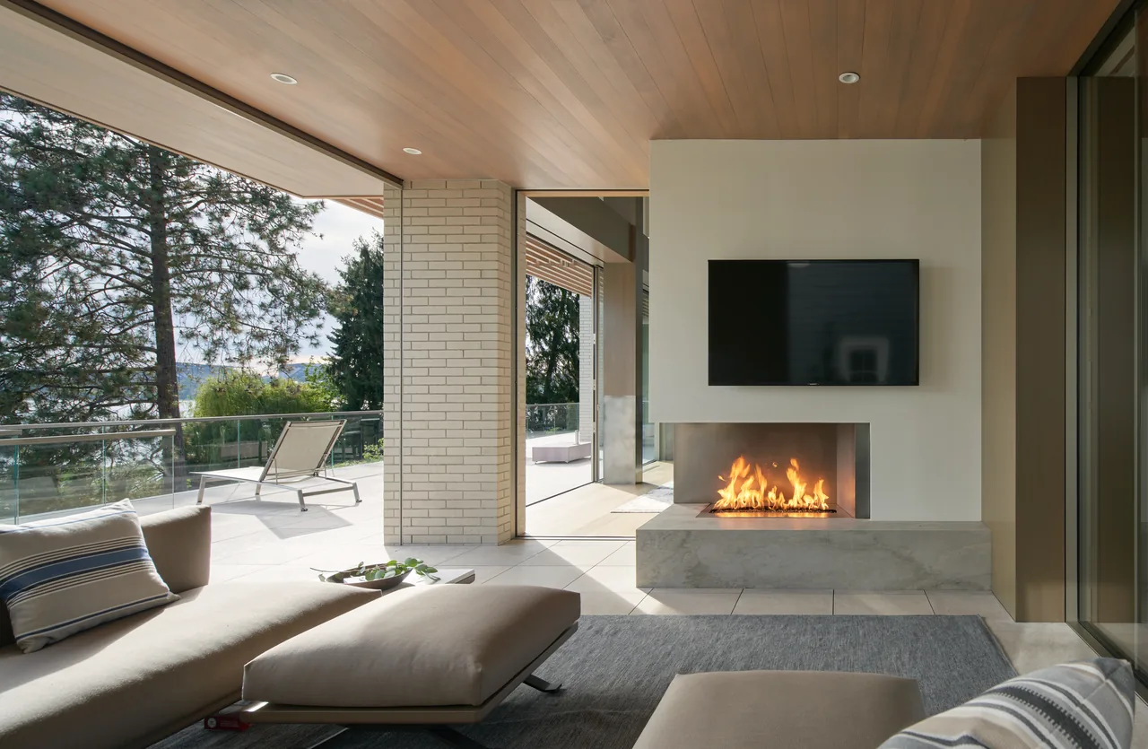Living area with fireplace and TV opens to a spacious outdoor deck with seating and greenery.