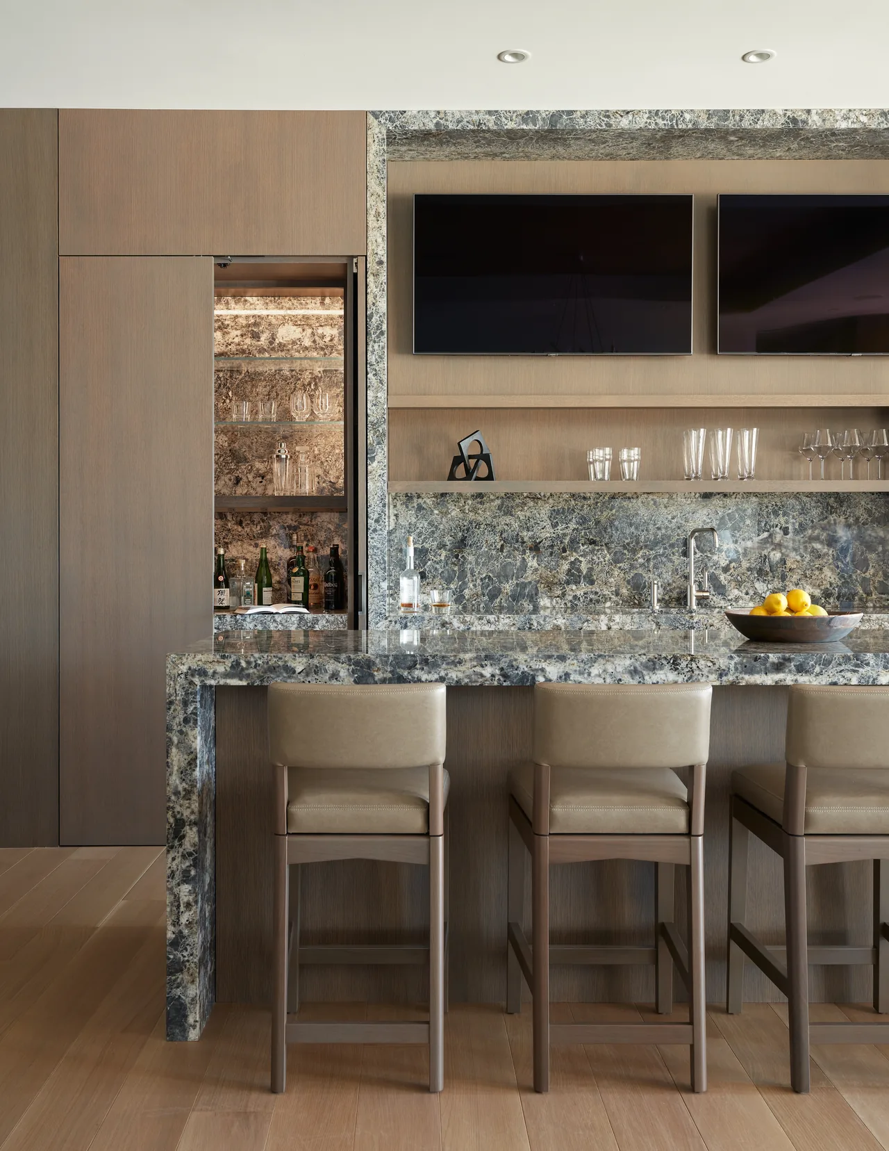 Union Bay Residence bar area featuring a stone countertop and backsplash with taupe leather bar stools and built-in shelving.