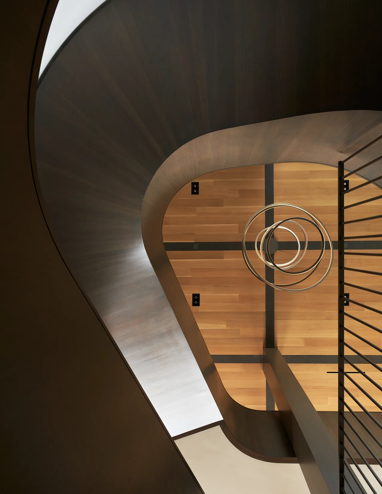 Curved wood staircase with circular ring pendant light and detailed wood ceiling in the Union Bay Residence.