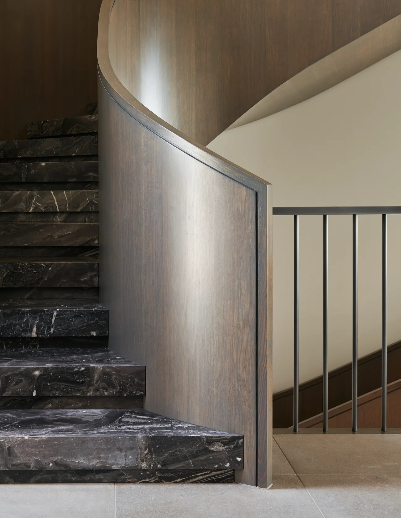The Union Bay Residence features a curved staircase with dark marble treads and a smooth wooden handrail and panel.