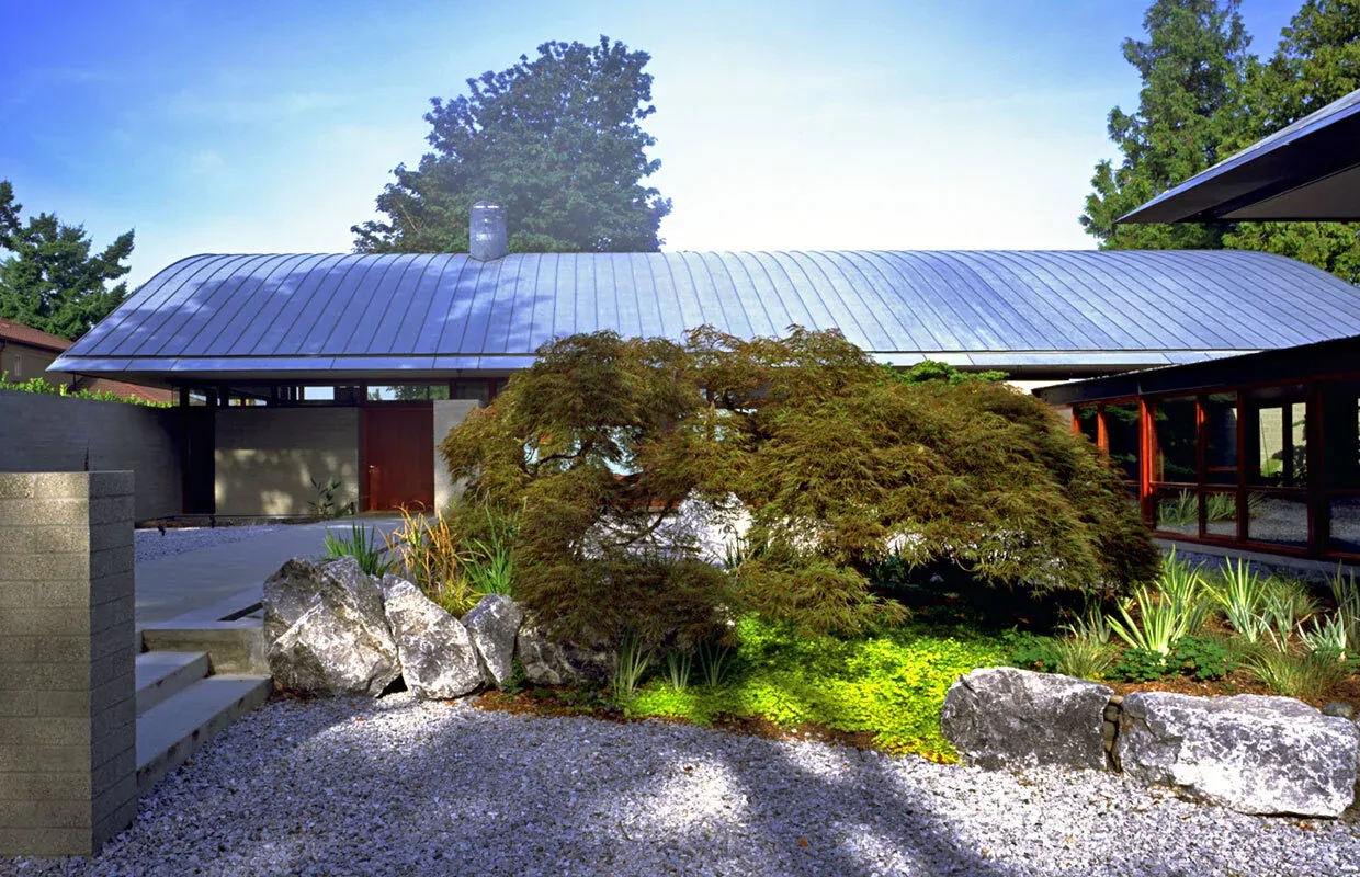 The Solbeck Residence features a curved metal roof with gravel ground cover and lush landscaping at the entry.