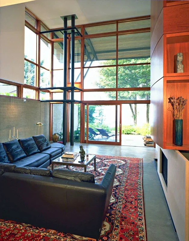 The Solbeck Residence living room features expansive glazing and wood-framed windows with a fireplace and leather seating.