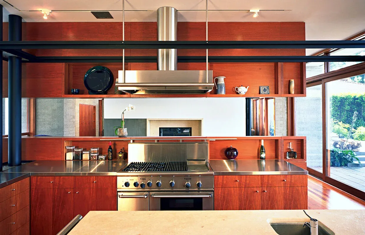 Kitchen of Solbeck Residence features stainless steel appliances and warm wood cabinetry with views to an outdoor living area.