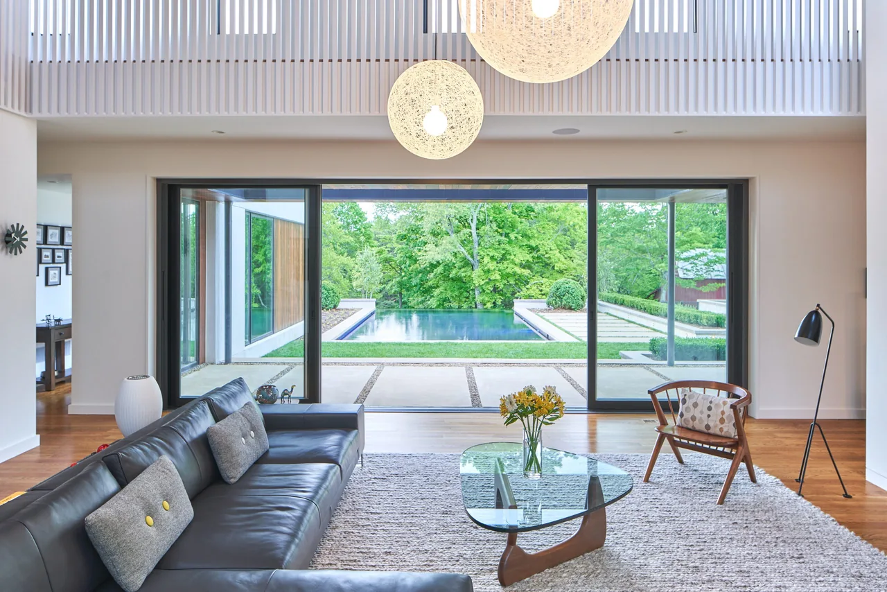 Open living space features a leather sectional and glass coffee table facing sliding glass doors to a courtyard with a pool and greenery.