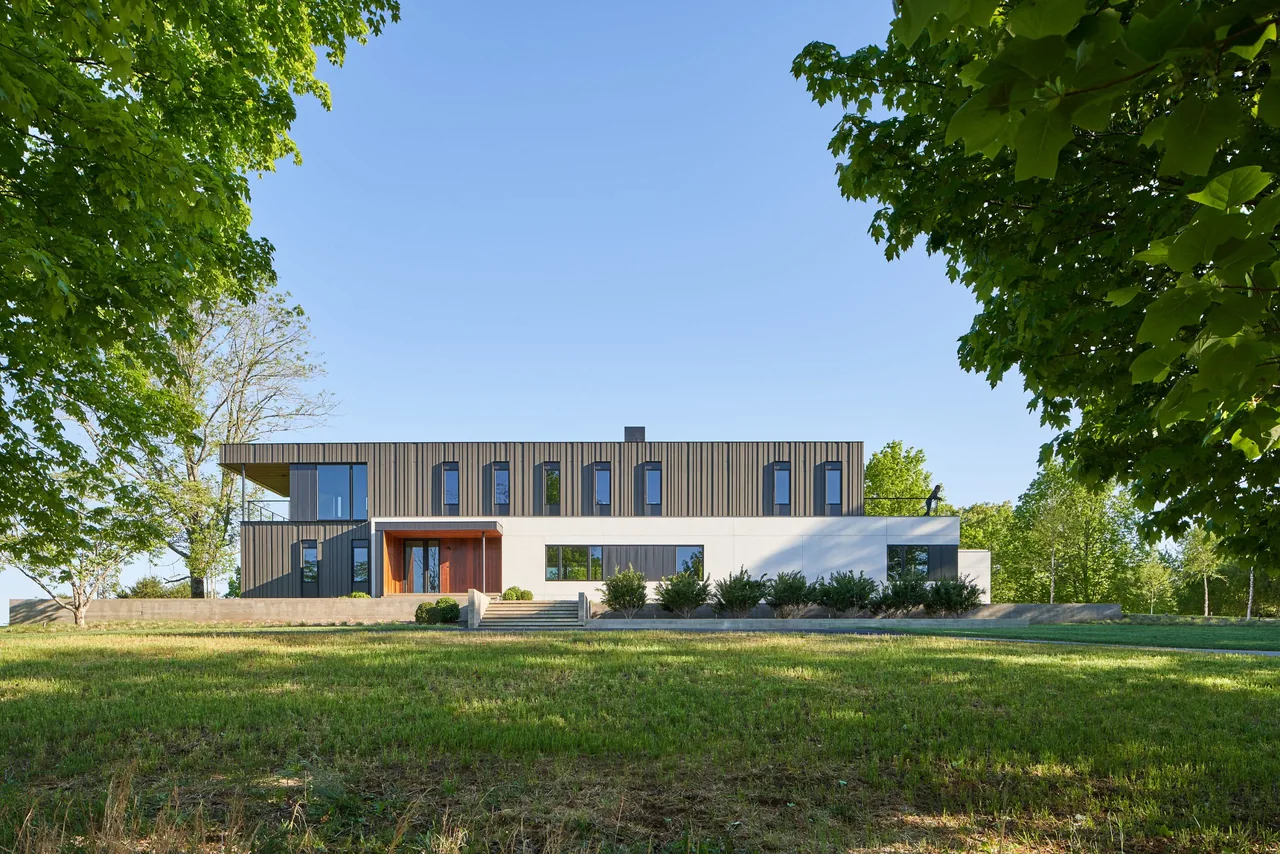 Two-story modern house with vertical siding and large windows framed by trees.