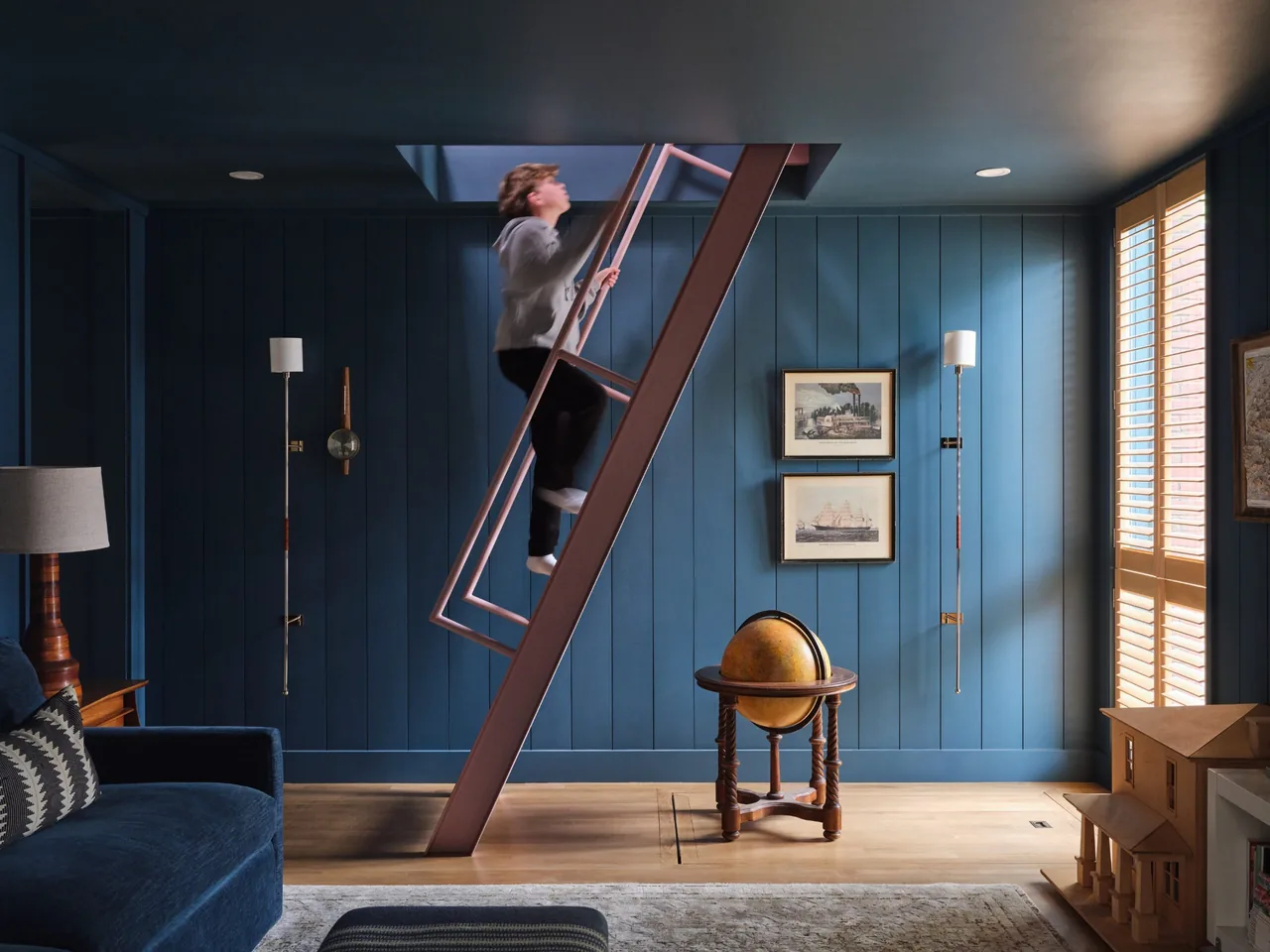 Interior view of a blue paneled living space with a ladder to a loft, framed artwork, and a wooden globe stand.