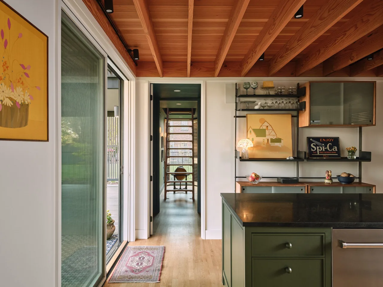 Kitchen space features a black countertop island, exposed wood ceiling beams, and wall shelving with decorative items and artwork.