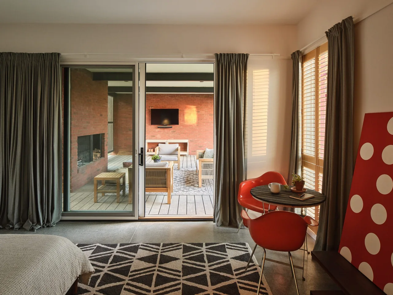 Bedroom opens to covered outdoor living space with fireplace and wood furniture at Morgan Street House.