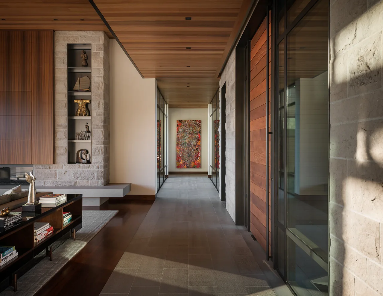 Modern hallway features wood ceiling, stone accents, and built-in shelving, with a vibrant artwork at the far end.