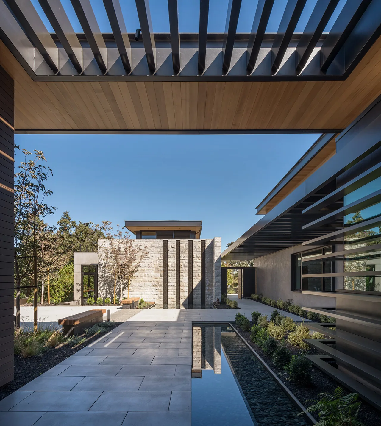 Courtyard of Portola Valley House features stone walls, a water feature, and pergola shading by SB Architects.