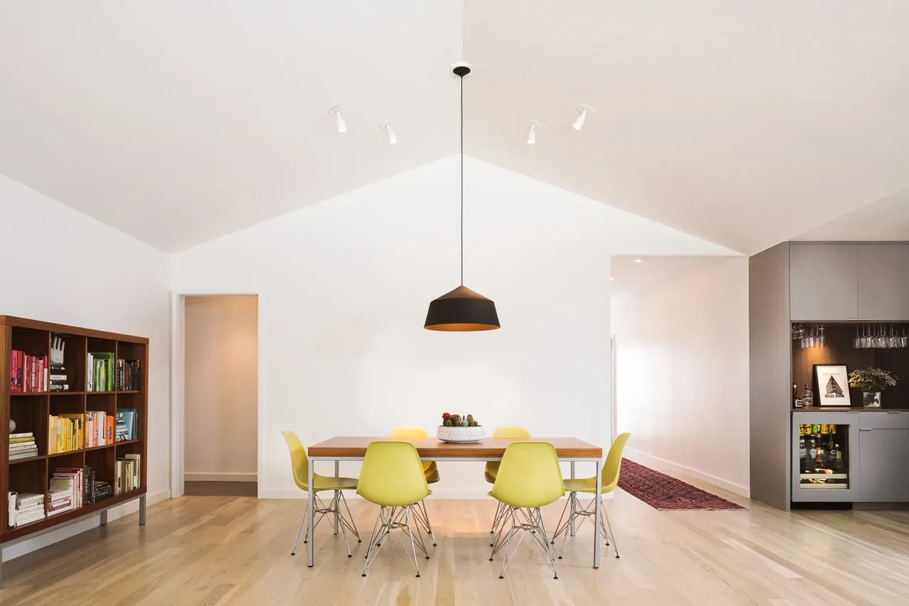 Dining space featuring yellow chairs around a wooden table and a black pendant light suspended from a vaulted ceiling.