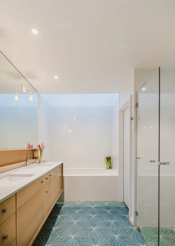Bathroom with wood vanity, patterned floor tile, built-in tub, and glass shower enclosure under a skylight.