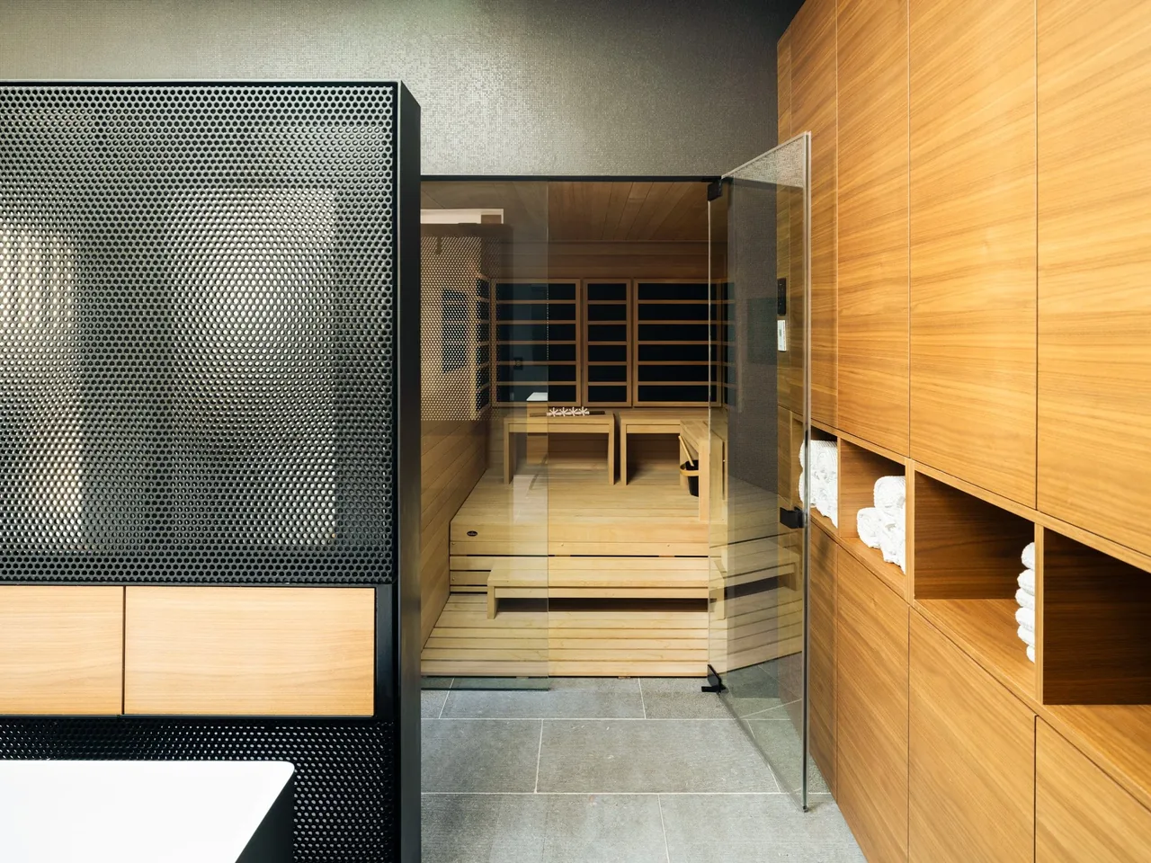 Sauna room interior with wooden benches and a glass door adjacent to wooden towel storage.