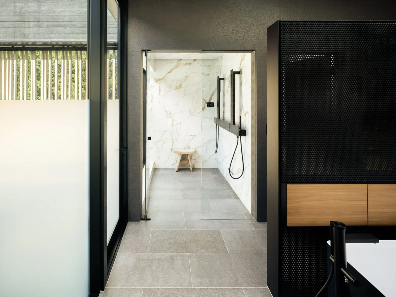 The Hunter Residence features a walk-in shower with marble walls and minimalistic black hardware.