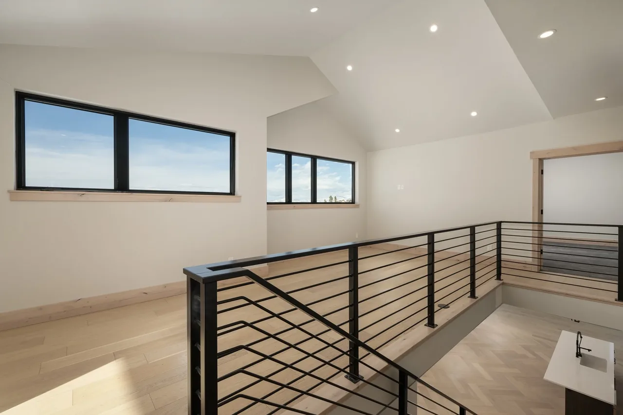 Multi-level interior space with black metal stair railing, light wood floors, and large black-framed windows.