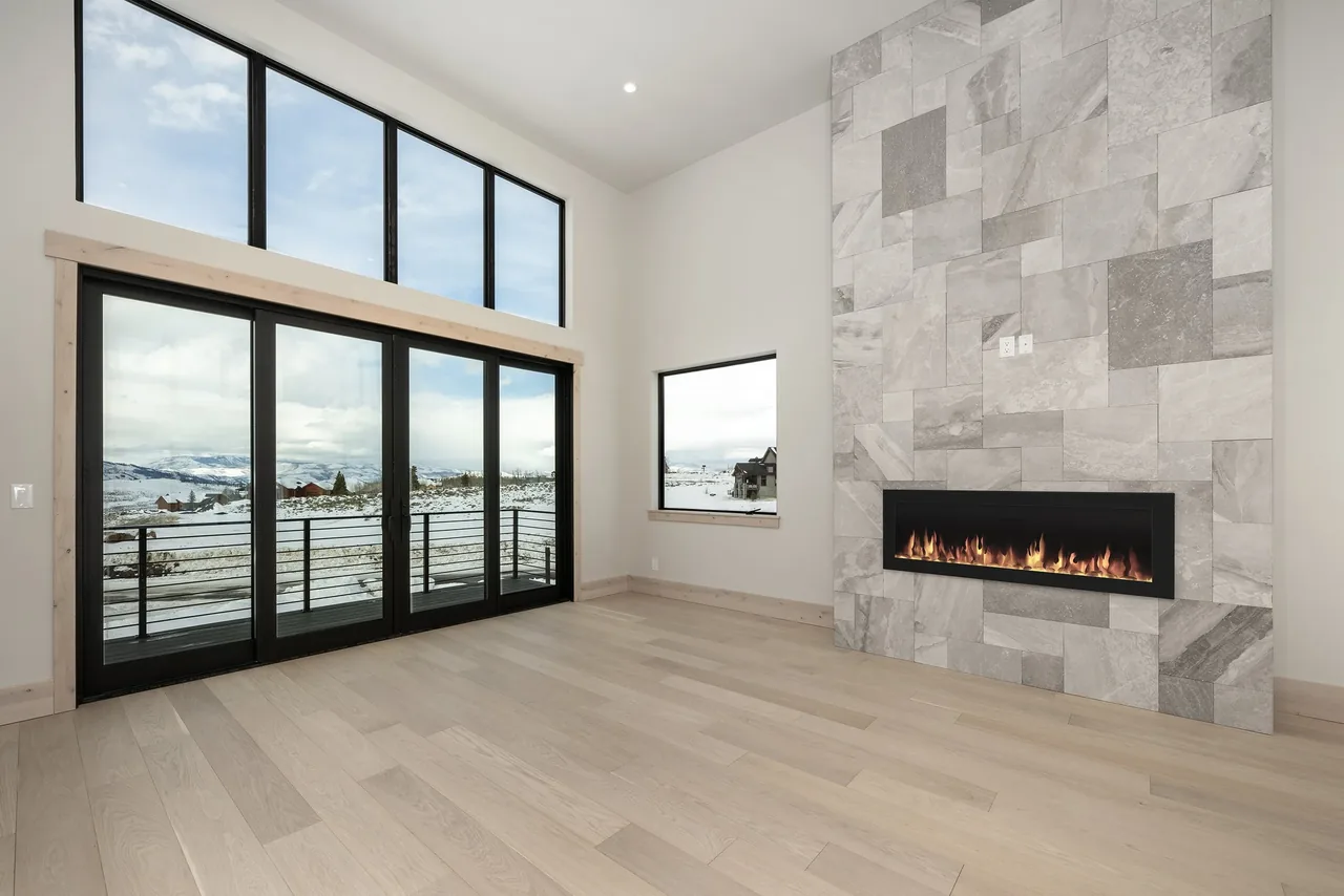 Living room features floor-to-ceiling sliding glass doors with black frames and a linear fireplace recessed in a textured stone wall.
