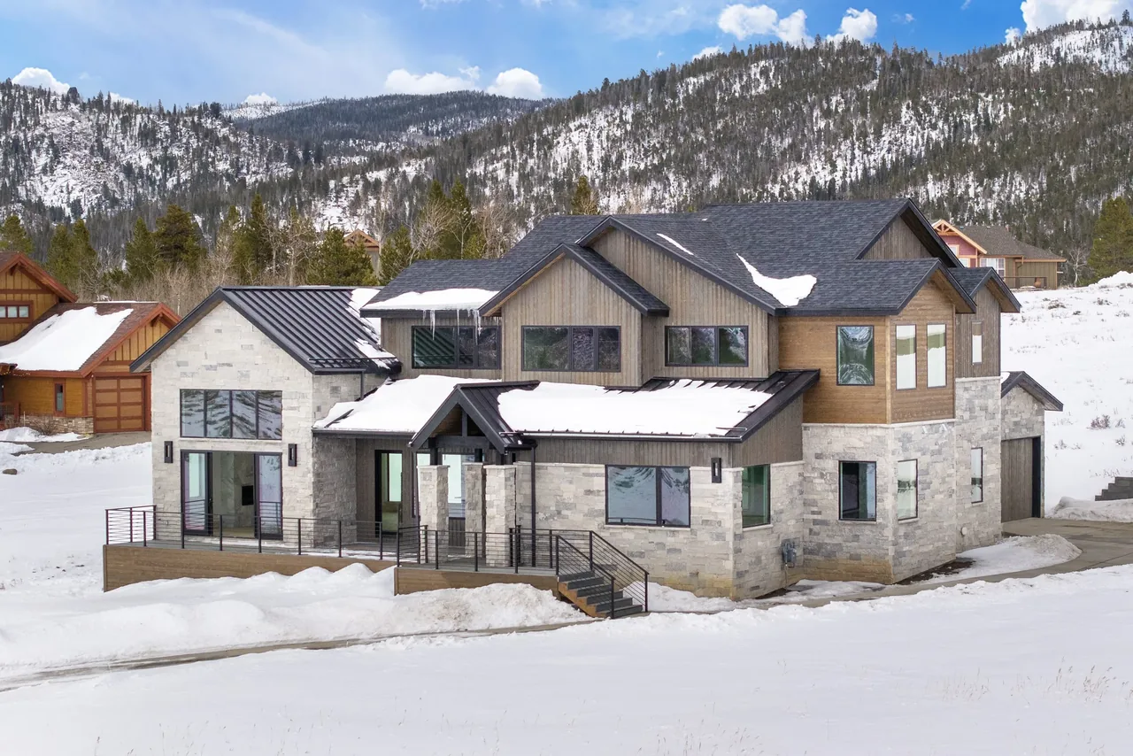 Slope-side Elegance features stone and wood exterior with multiple gable roofs amid a snowy mountain setting.