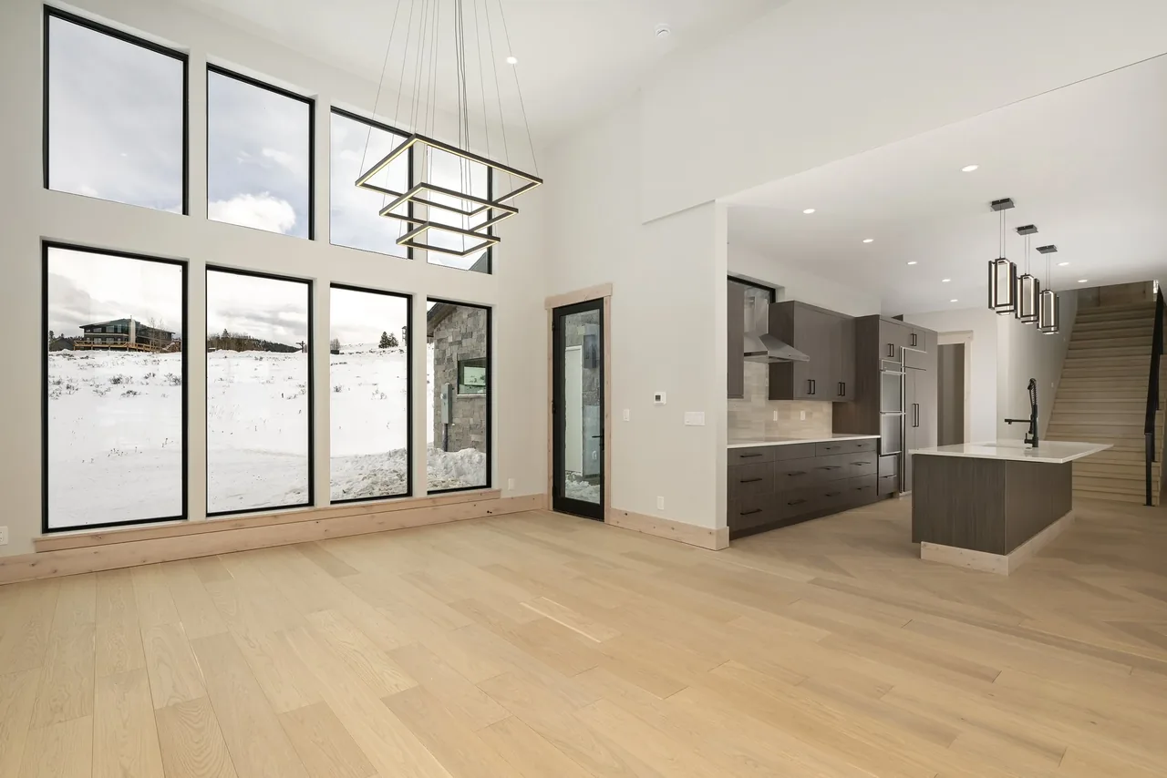 Open space with floor-to-ceiling windows, modern kitchen, and geometric pendant lighting under vaulted ceilings.