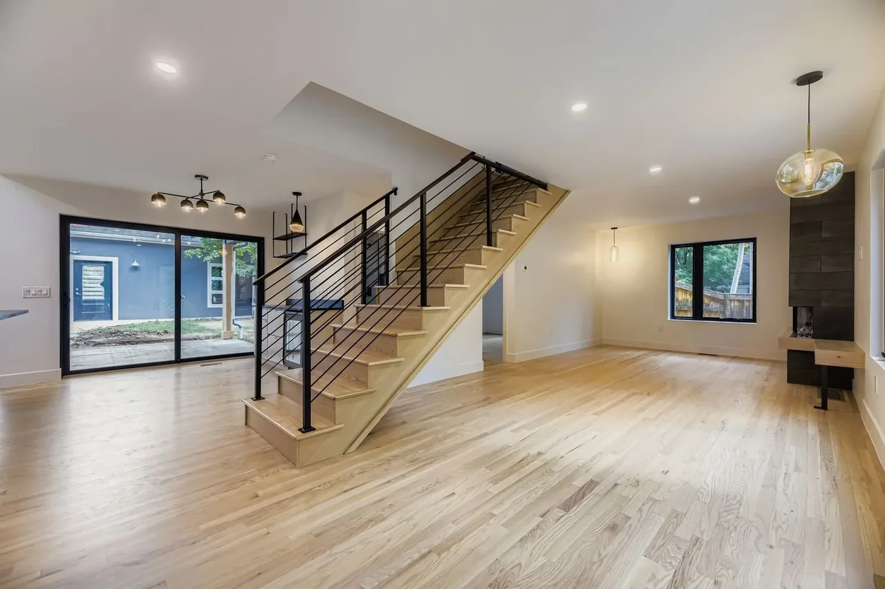 Open floor plan living area features light wood floors, black metal stair railing, and sliding glass doors to an outdoor space.