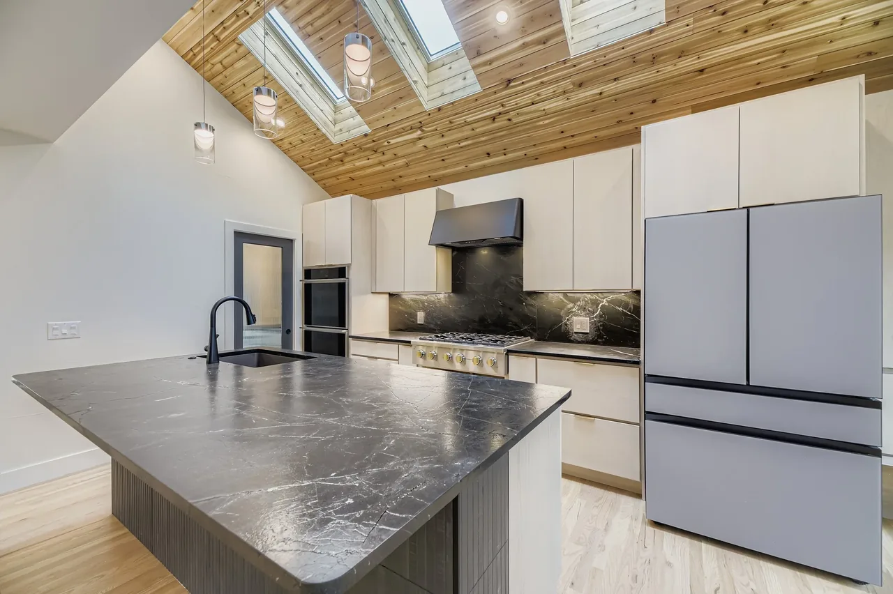 The kitchen features a vaulted ceiling with skylights, black stone countertops, and light cabinetry.