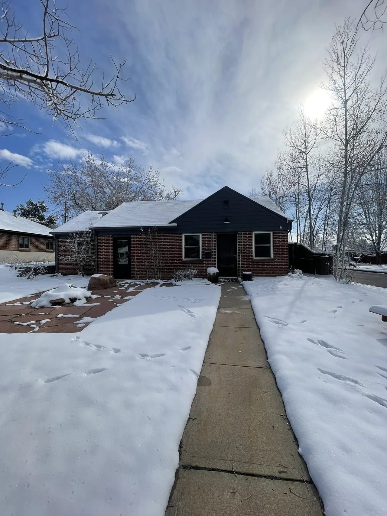 Single-story brick house with a dark front gable and a concrete walkway through a snow-covered yard.