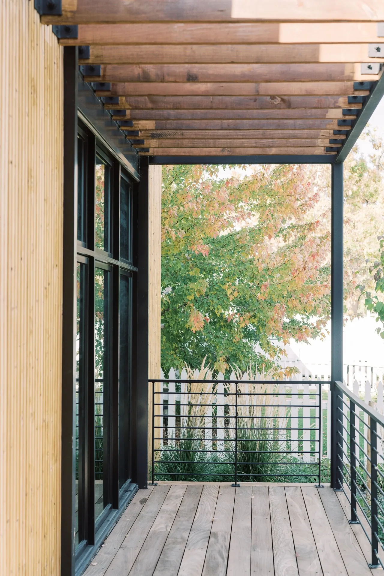 Covered porch with vertical wood siding, metal pergola, and black wire railing in the Louisville Net-Zero Residence.