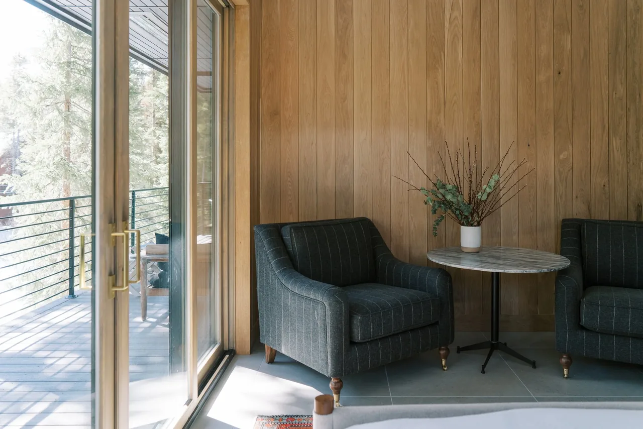 Living area with two upholstered armchairs, a marble round table, and wood paneling beside a glass sliding door to the outside deck.