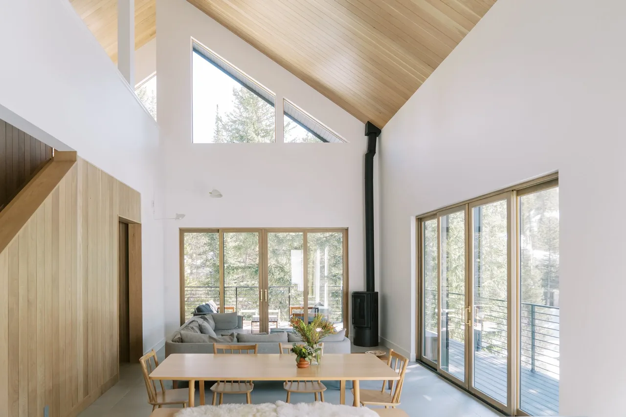 The Winter Park Residence features a spacious dining and living area with a vaulted wood ceiling and floor-to-ceiling wood-framed glass doors opening to outdoor spaces.