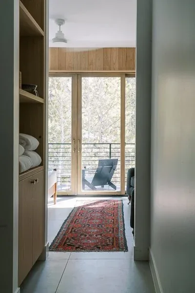 Hallway with wood paneling and glass entry door opens to a balcony overlooking a forest.