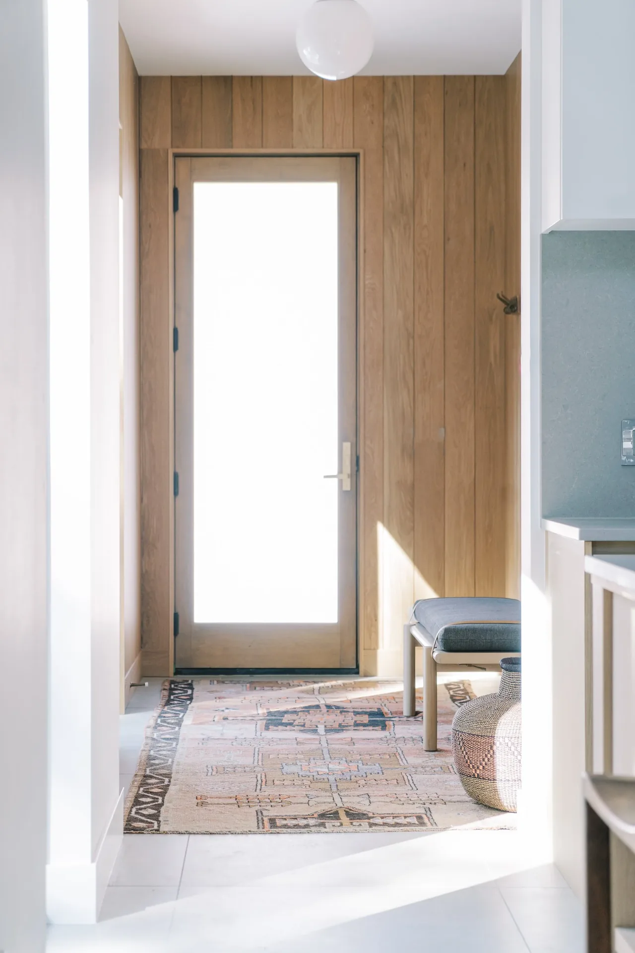 Entry hallway features vertical wood panel walls, a glass door, and a patterned rug placed on tiled flooring.