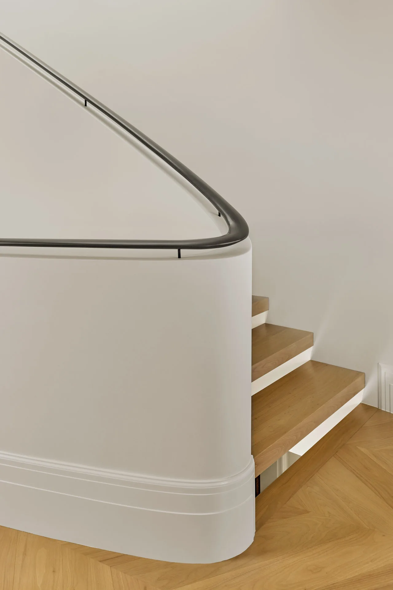 The staircase features wooden treads, a curved white wall, and a minimalist black handrail at Seacliff Residence.