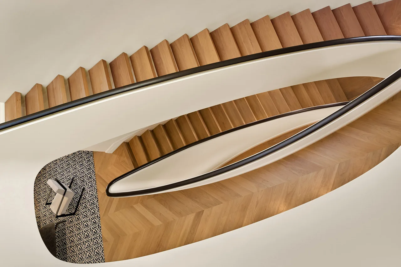 Curved wooden staircase at Seacliff Residence with black handrails and patterned rug at the base.