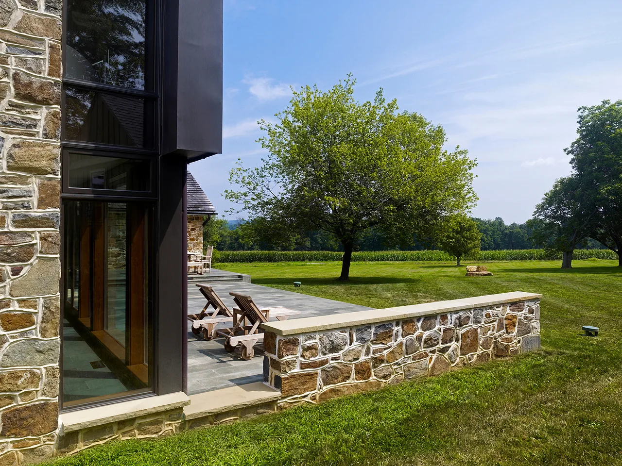 The Elverson Addition features a stone and metal exterior with large windows opening onto a stone patio and surrounding greenery.